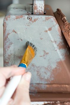 a person holding a paintbrush in front of a rusted piece of metal structure