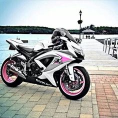 a white and pink motorcycle parked next to a body of water with a pier in the background