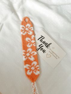 an orange and white beaded tie sitting on top of a bed next to a thank you card