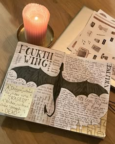 an open book sitting on top of a wooden table next to a candle and paper