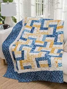 a blue and yellow quilt sitting on top of a white couch next to a window