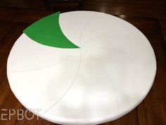 a white table with a green leaf on it's top sitting on a wooden floor