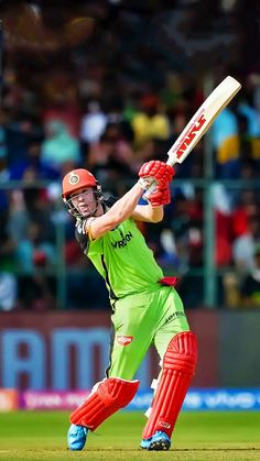 a man in green and red batting on a field with people watching from the stands