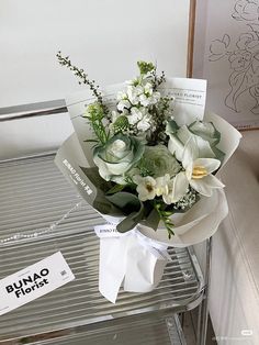 a bouquet of white flowers sitting on top of a metal shelf next to a sign