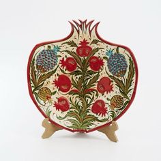 a red and white vase sitting on top of a wooden stand next to a white wall