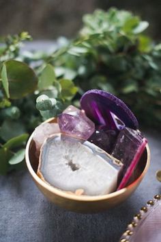 an assortment of crystals in a wooden bowl on a table next to plants and beads