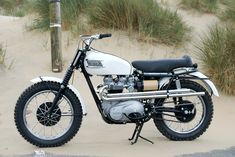 a white motorcycle parked on top of a sandy beach next to grass and sand dunes