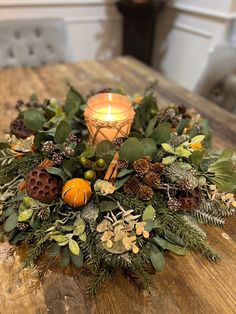 a candle that is sitting on top of a table with greenery and pine cones