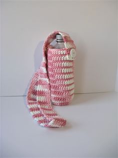 a pink and white crocheted purse with a bottle holder attached to the strap