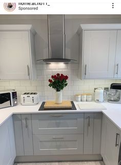 a kitchen with white cabinets and gray counter tops, flowers in a vase on the stove