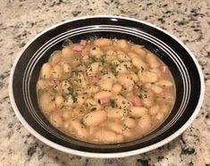 a black bowl filled with beans and meat on top of a granite countertop next to a bottle of wine