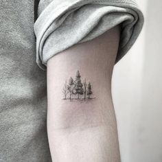 a small tree tattoo on the left inner arm and shoulder, with trees in the background