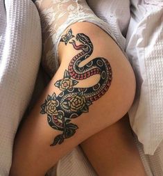 a woman laying in bed with a snake tattoo on her thigh and leg, next to a pillow