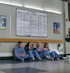 four people in scrubs sitting on the floor next to a wall with a sign