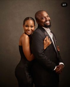 a man and woman are posing for a photo in front of a dark background they are both smiling at the camera