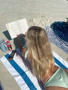 a woman sitting on top of a towel next to an open book and cell phone