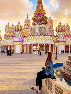 a woman sitting on the edge of a fountain in front of a building with domes