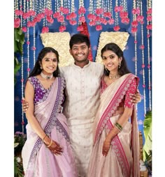 three people standing next to each other in front of a wall decorated with flowers and garlands