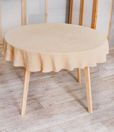 a round table with a beige cloth on it in front of two wooden chairs and a wall