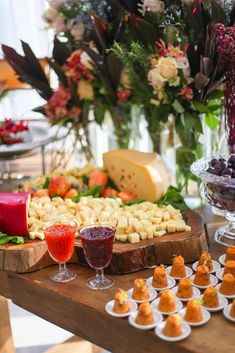 an assortment of appetizers and cheeses on a wooden table with flowers in the background