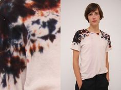 a boy standing in front of a white wall next to a tie dyed t - shirt