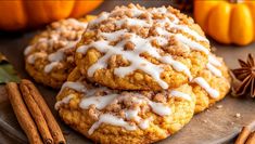 two cookies with white icing and cinnamon on a plate next to an orange pumpkin