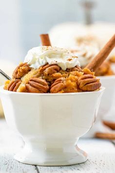 a white bowl filled with dessert and topped with whipped cream, pecans and cinnamon sticks