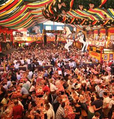 a large group of people are dancing at an outdoor event with colorful flags and decorations on the ceiling