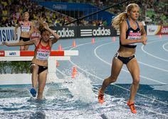 two women in bikinis are running through water on a track with an audience watching