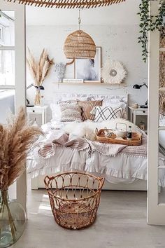 a white bedroom with wicker furniture and baskets on the bed, along with plants in glass vases