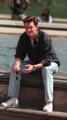 a man sitting on the edge of a fountain with his hands in his pockets and looking off into the distance