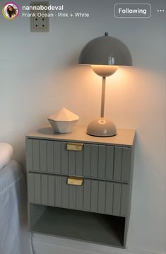 a white lamp sitting on top of a gray cabinet next to a bed and nightstand