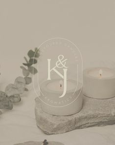 two white candles sitting on top of a rock next to rocks and succulents