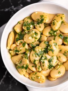 a white bowl filled with pasta and parsley on top of a marble countertop