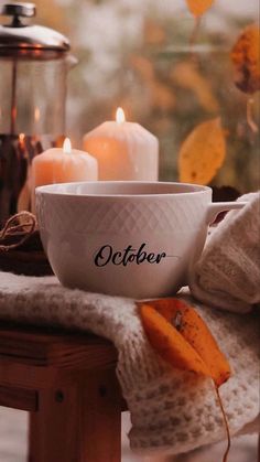 a white bowl sitting on top of a wooden table next to two candles and a blanket