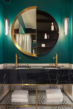 a bathroom with green walls and marble counter tops, gold fixtures and a round mirror