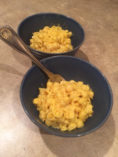 two bowls filled with macaroni and cheese next to a spoon on a counter