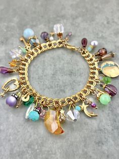 WHAT IT IS:  A "Moonlit Treasures" themed charm bracelet heavily adorned in shades of purple, aqua, seafoam, and topaz. A large vintage Swarovski moon is surrounded by vivid, sparkly dangles, each and every one of which is crafted from vintage pieces--brass charms, Czech glass, lucite, and an array of vintage Swarovski crystals in various shapes and sizes. THE SPECS: - 7.5 inches total length. - Lobster clasp closure. - 20mm vintage Swarovski crystal moon.  WHY IT'S SPECIAL: Some of our fondest memories are of stargazing from our California wine country mountaintop, away from traffic and streetlights and the rest of the world. We created "Moonlit Treasures" to capture the essence of those clear, starry nights where the crisp nighttime air wraps us in a cool embrace and the moon illuminates Artisan Jewelry Handmade, Crystal Moon, Starry Nights, California Wine, Brass Charms, Crown Jewels, Swarovski Jewelry, Add Ons, Diy Charms