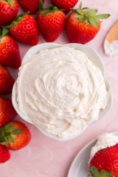 a bowl of whipped cream next to some strawberries on a pink surface with spoons