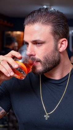 a man drinking from a wine glass with a cross necklace on it's neck