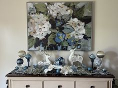 a painting on the wall above a dresser with blue and white decorations in front of it