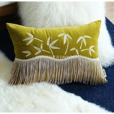 a green pillow with white flowers and fringes on the bottom is sitting on a blue rug