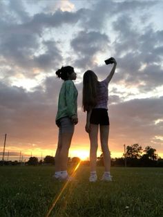 two girls are standing in the grass with their arms up and looking at the sky