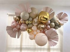 balloons are hanging from the ceiling in front of a window with white and gold decorations