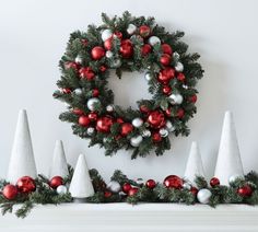 a wreath and christmas decorations on a mantel with cones, balls and ornaments around it