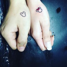 two people holding hands with tattoos on their fingers and one has a mickey mouse tattoo