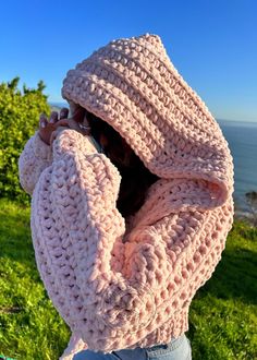 a woman wearing a pink knitted hoodie looking out at the ocean with her hands on her hips