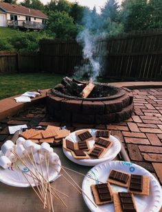 some food is laying out on plates near a fire pit with marshmallows