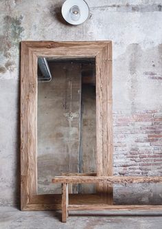 a wooden mirror sitting on top of a wall next to a bench and light fixture