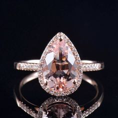 an engagement ring with a pear shaped morganite surrounded by pave diamonds on a black background